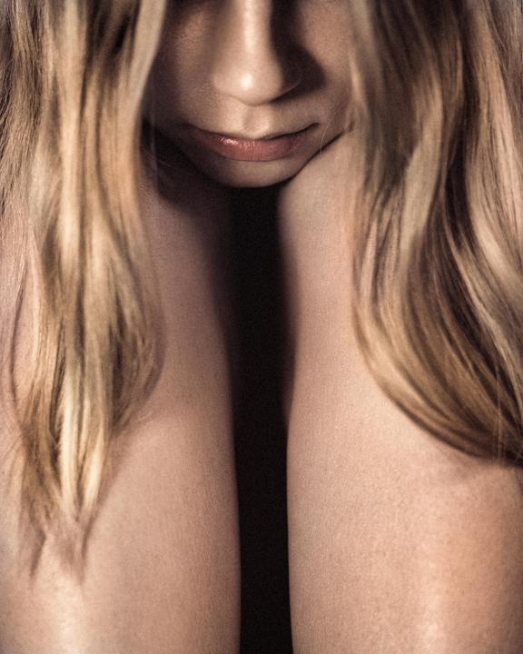A woman's face is partially obscured by her long hair, with her chin resting on her hand.