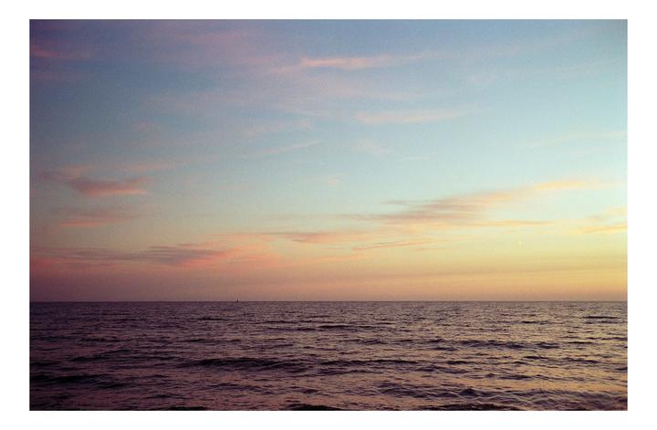 The ocean stretches to the horizon under a colorful sky at dusk.