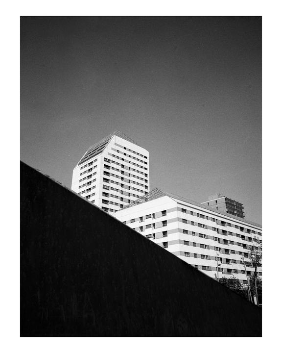 Two tall buildings are visible behind a dark, diagonal wall.