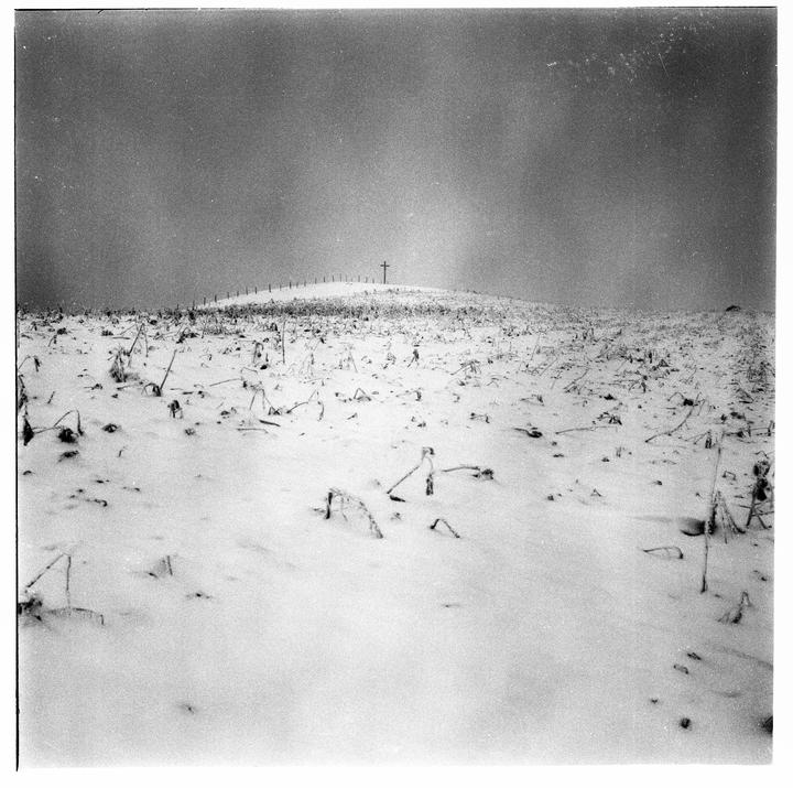 A snow-covered field with a cross on a hill under a hazy sky.