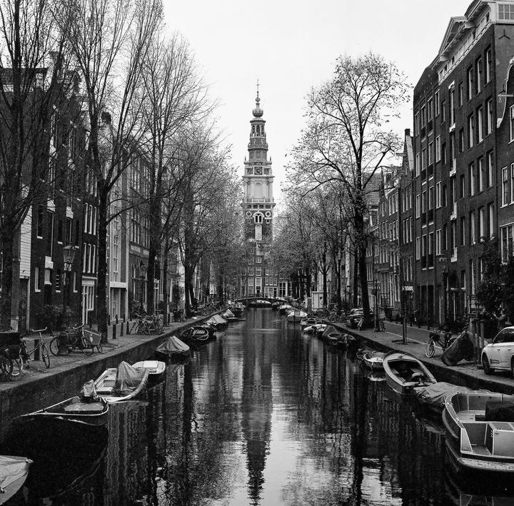 A canal lined with boats and buildings leads to a tall clock tower in Amsterdam.