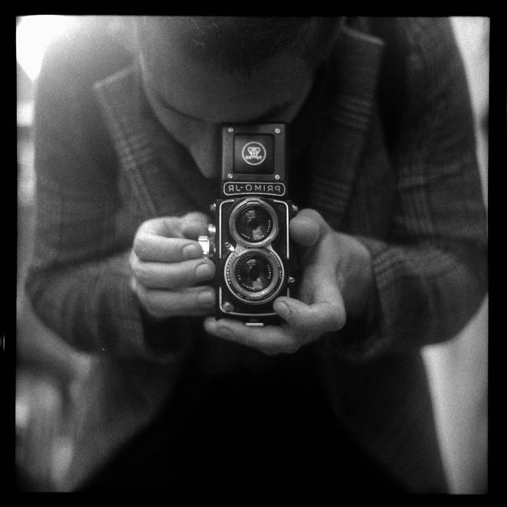 A man looks down into the viewfinder of a twin-lens reflex camera.