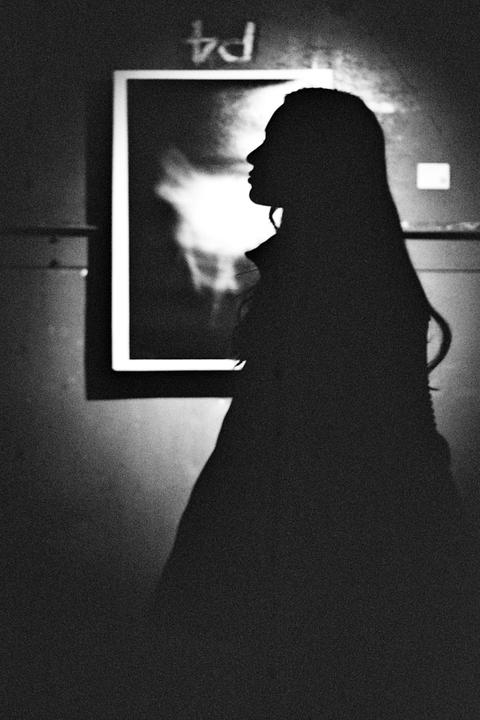 A woman's silhouette is visible in profile against a bright, framed image on a wall.