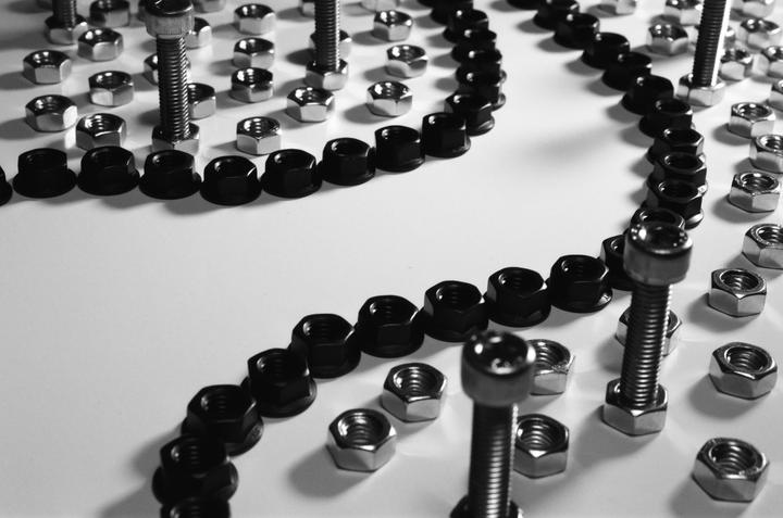 A still life image shows a pattern of nuts and bolts arranged on a white surface.