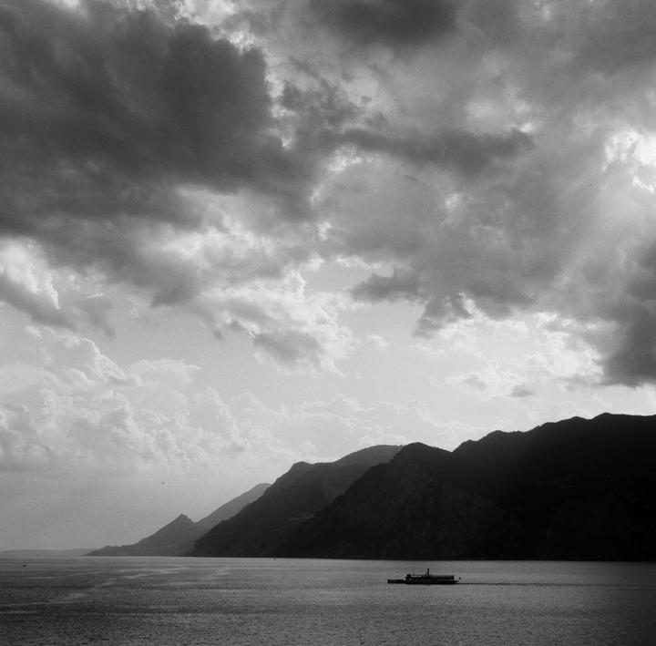 A boat travels on a body of water with mountains in the distance under a cloudy sky.