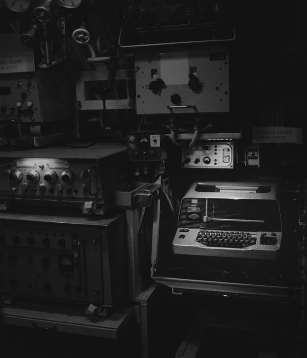 A radio station with various electronic equipment and a teletypewriter is visible in a dark room.