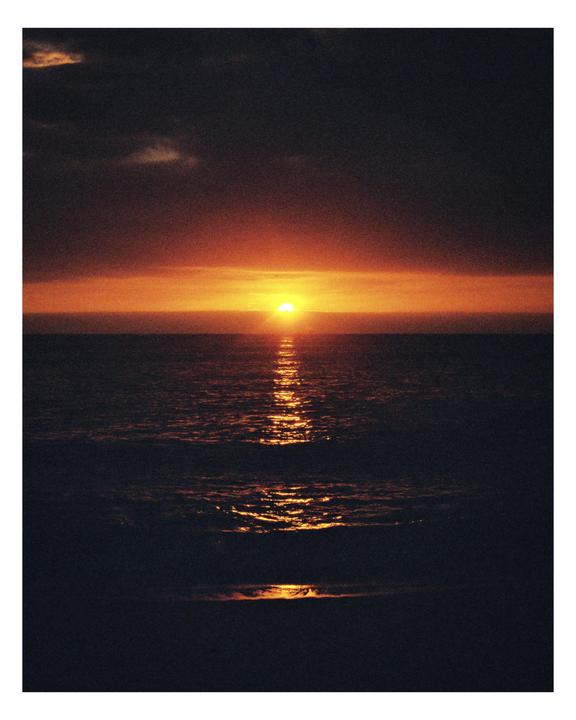 The sun sets over the ocean, casting an orange glow on the water.