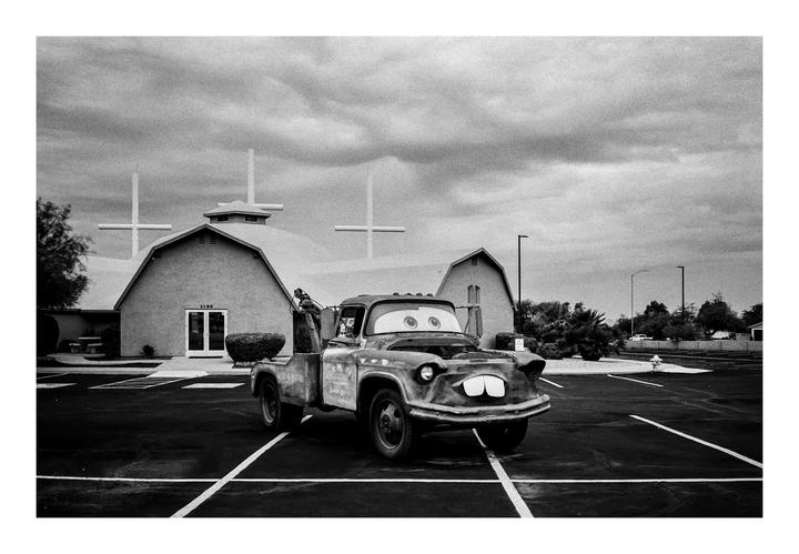 A tow truck with cartoon eyes and teeth is parked in front of a church with two crosses on its roof.