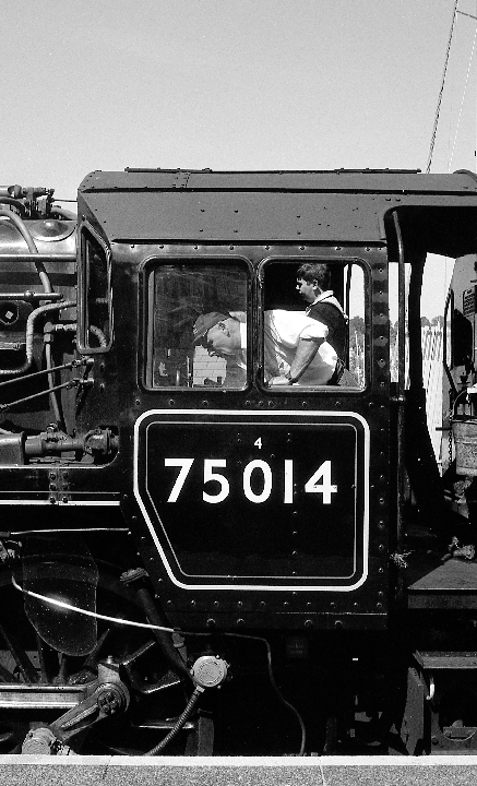 Two men are visible through the windows of a large train engine with the number 75014 on its side.
