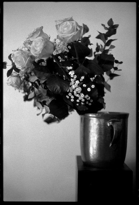 A bouquet of roses and baby's breath is arranged in a metal mug on a dark surface.