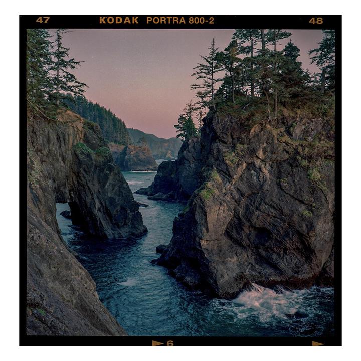 A body of water flows between two rocky cliffs with trees on top.