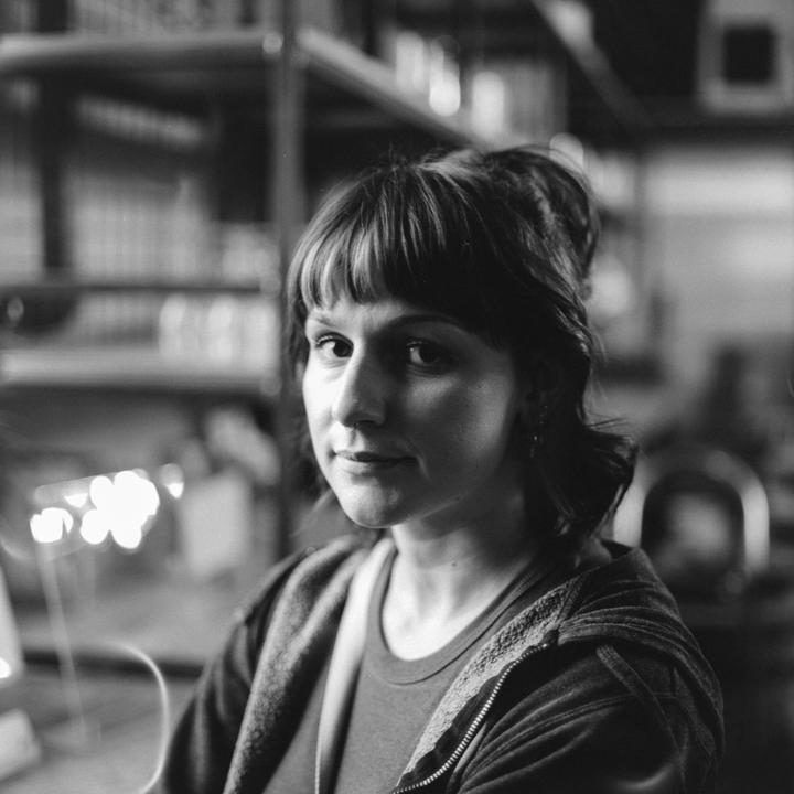 A woman with bangs and a nose ring looks at the viewer.