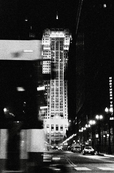 A tall building with many windows is visible at night, with a street and cars in the foreground.