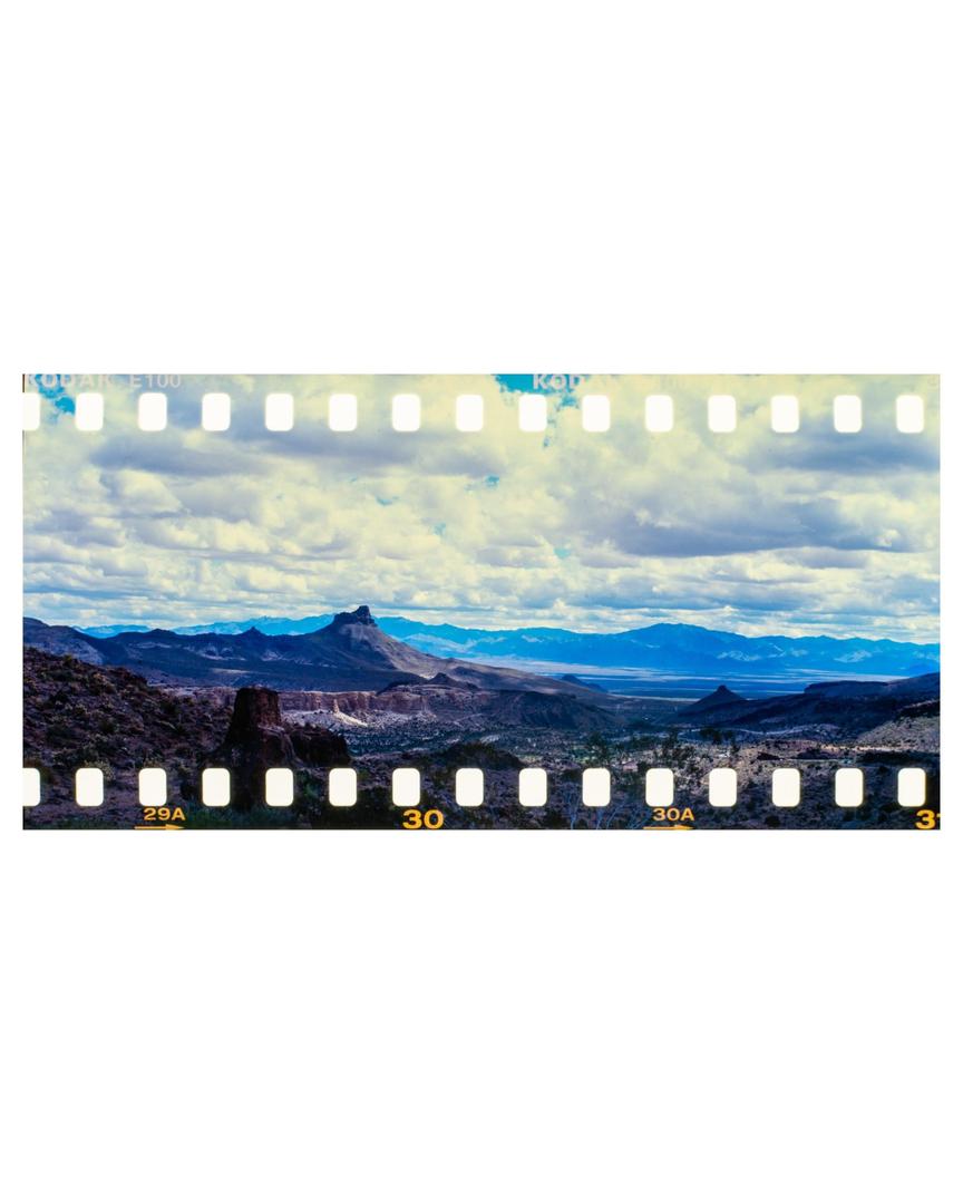 A vast desert landscape with mountains under a cloudy sky is visible.