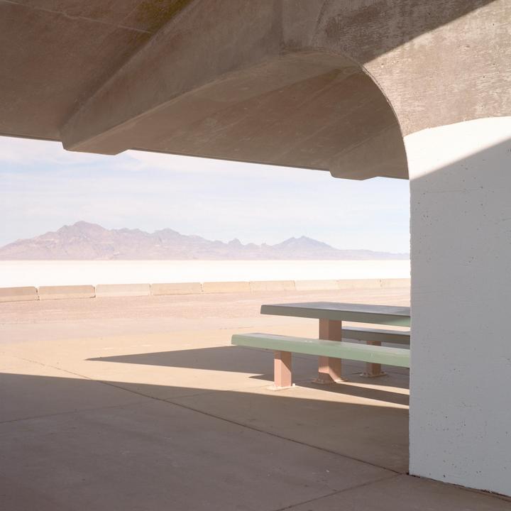 A picnic table sits under a concrete overhang, looking out onto a vast, flat landscape with mountains in the distance.