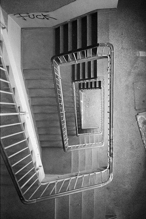 A black and white overhead view shows a spiral staircase with graffiti on the wall.