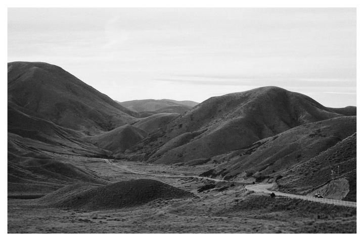 A winding road cuts through a valley surrounded by rolling hills under a bright sky.