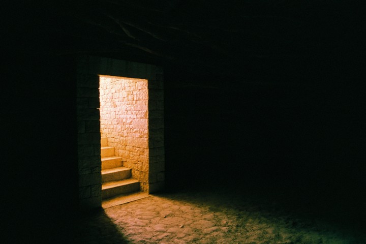 A stone doorway with steps leads into a brightly lit space from a dark room.