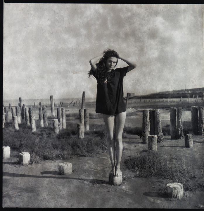 A woman stands on a wooden post in a dried lake bed surrounded by many other posts.