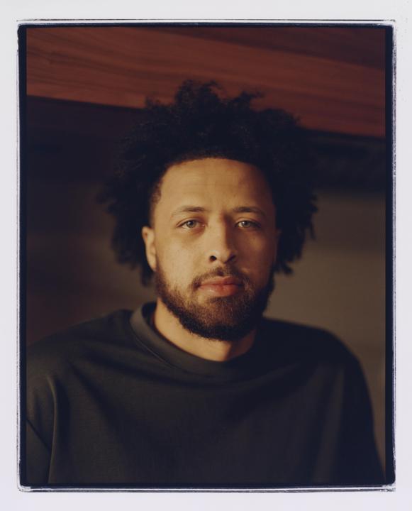 A man with curly hair and a beard looks directly at the viewer in a headshot.