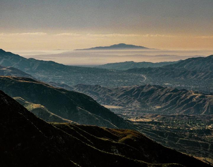 A hazy valley is visible between layers of mountains at sunrise.