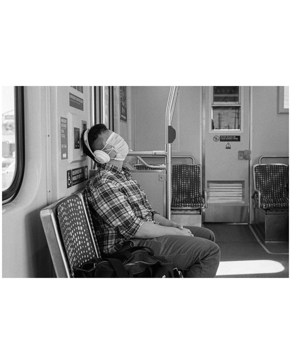 A man wearing a face mask and headphones is sleeping on a train.