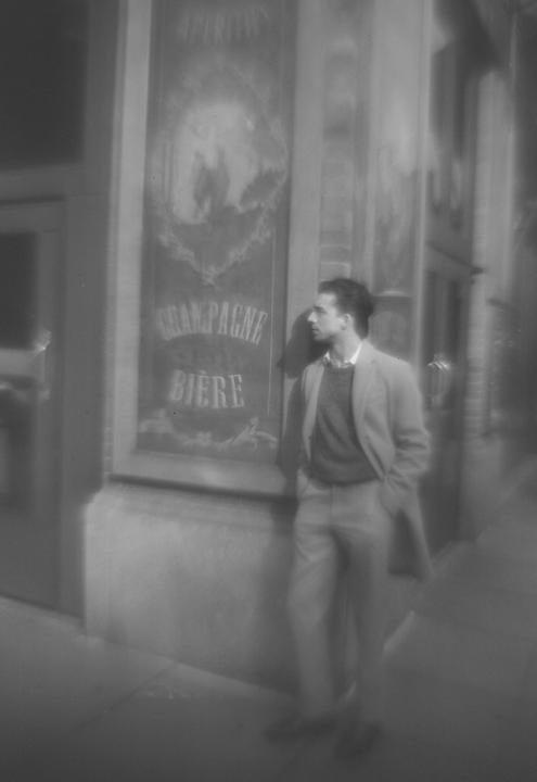 A man stands on a sidewalk next to a building with a sign that reads "Champagne Biere."