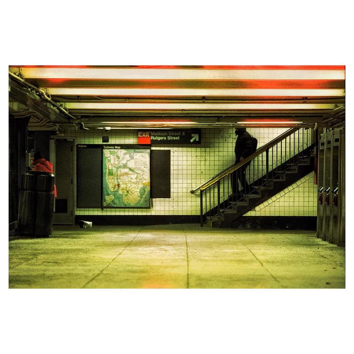 A person walks up a staircase in a subway station with a subway map on the wall.
