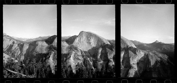 A panoramic black and white landscape shows a large rock formation with a rounded top, surrounded by other mountains and a forest.