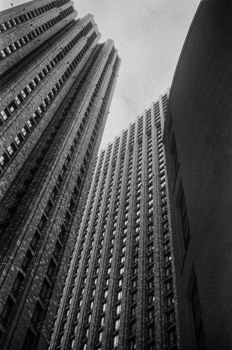 Three tall buildings with many windows are seen from a low angle, with one building curving on the right.