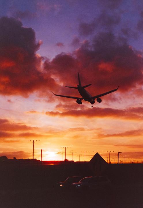 A passenger airplane is silhouetted against a vibrant sunset sky with clouds.