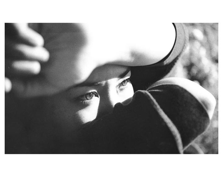 A woman's eyes are visible as she covers her face with her arm and clothing.