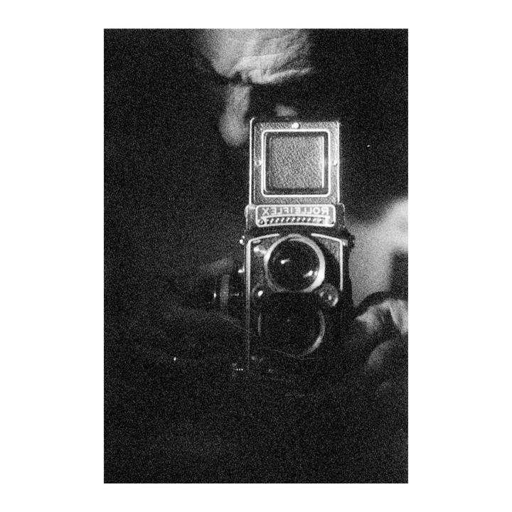 A Rolleiflex camera is held up, with its name visible in reverse.