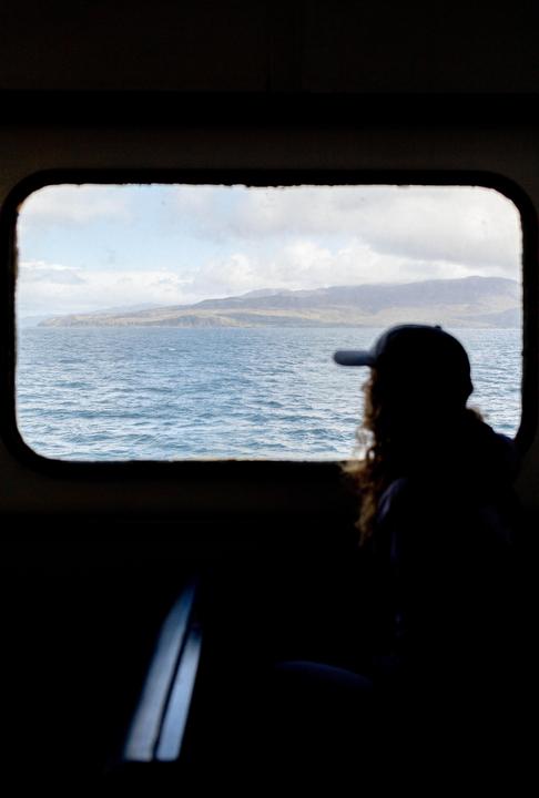 A person in silhouette looks out a window at a body of water and distant land.