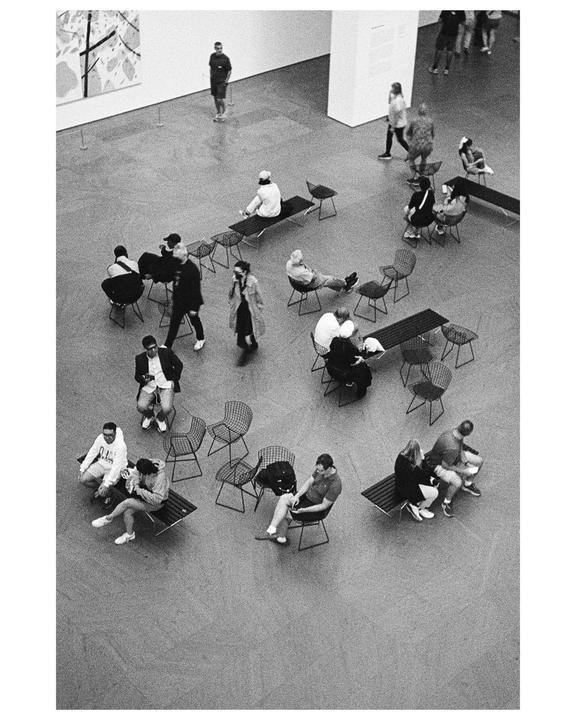 A high-angle view shows people sitting and standing in a large room with modern art on the wall.