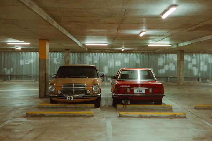 Two vintage cars are parked facing opposite directions in an underground parking garage.