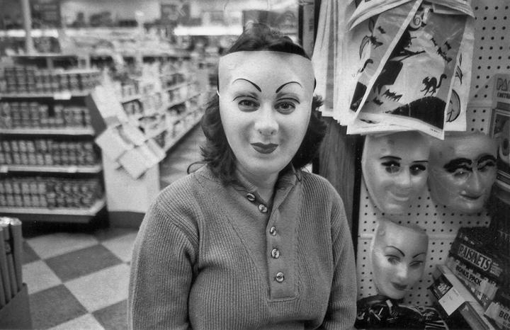 A woman wearing a mask stands in a store aisle next to a display of other masks.