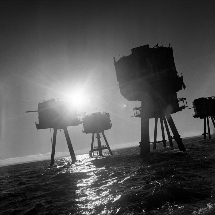 The sun shines brightly behind several large structures standing in the ocean.