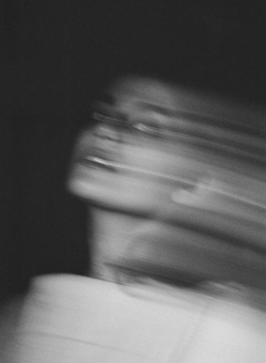 A blurry portrait of a person with glasses is visible against a dark background.