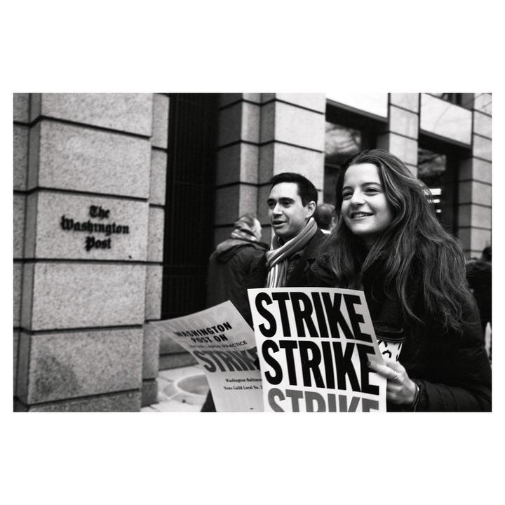 A woman and a man are holding "strike" signs in front of The Washington Post building.
