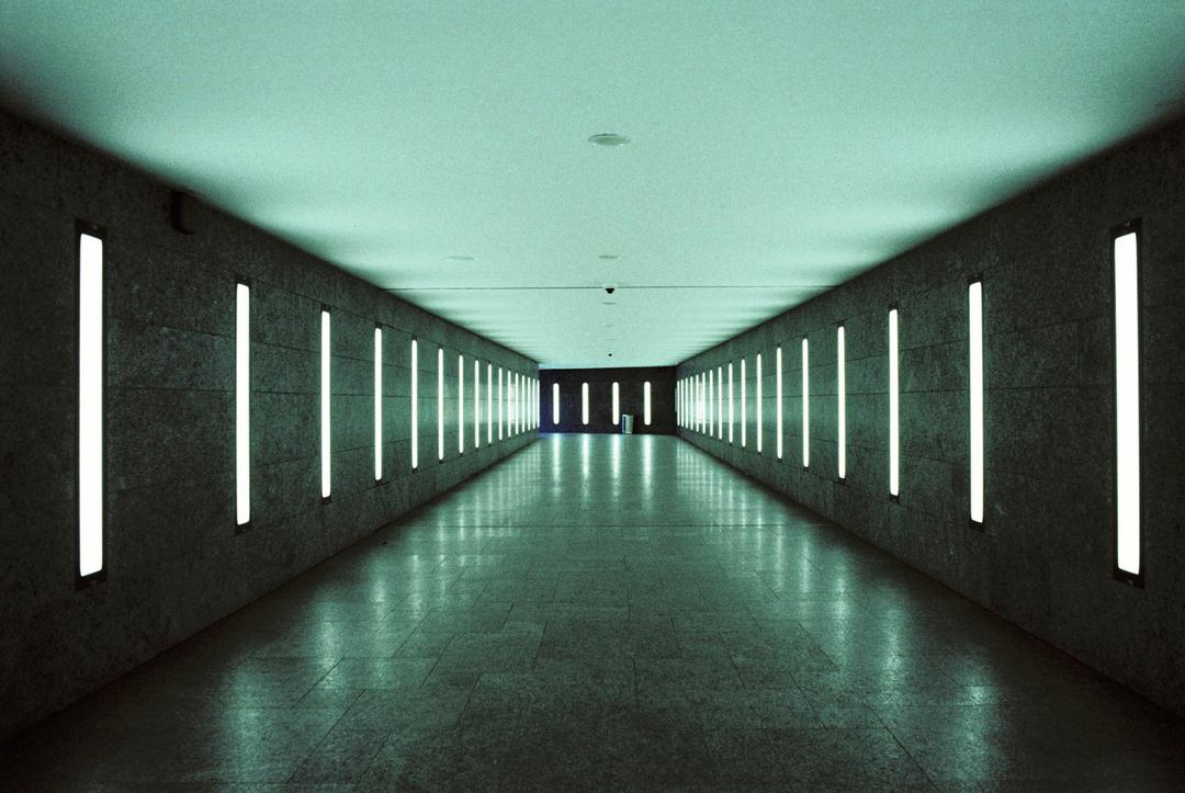 A long, empty subway tunnel is illuminated by vertical fluorescent lights on both walls.