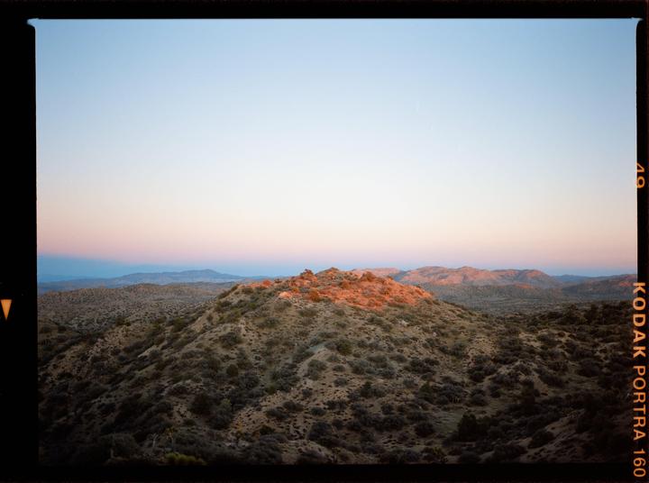 A desert landscape with hills and mountains is illuminated by the setting sun.