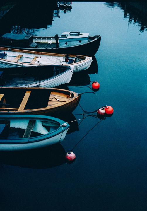 Several boats are moored in dark water with red buoys floating nearby.