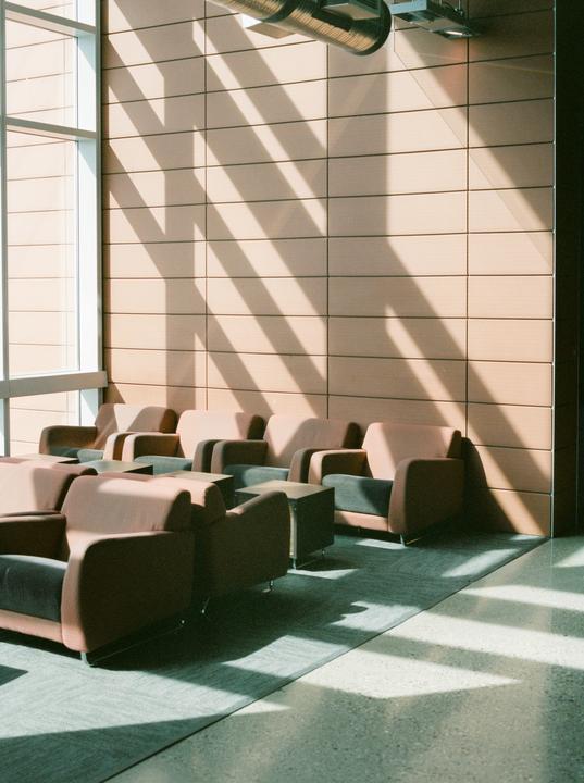 Sunlight streams through a large window, casting striped shadows across a wall and a row of armchairs in a waiting area.