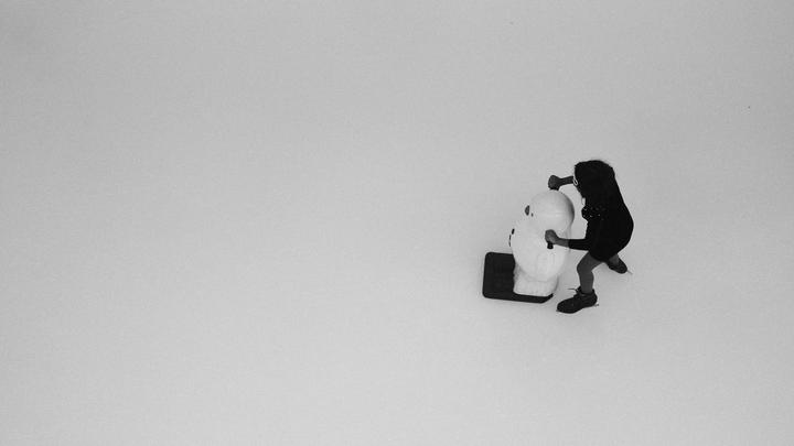 A child on ice skates pushes a snowman-shaped ice skating aid across a white surface.