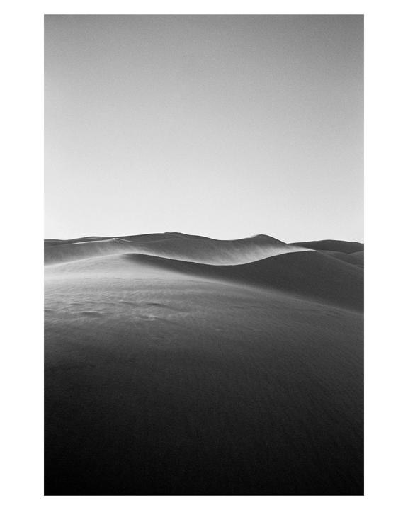 Wind blows across sand dunes under a bright sky.