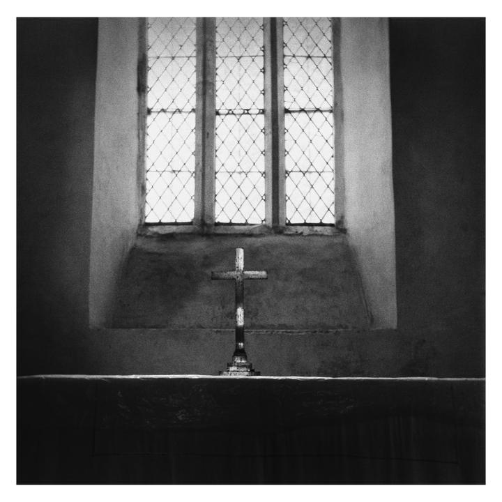 A cross stands on a surface in front of a large window with diamond-patterned panes.