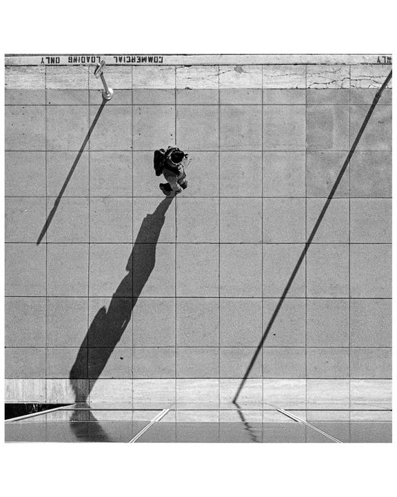 A person walks on a tiled sidewalk with a long shadow stretching out in front of them.