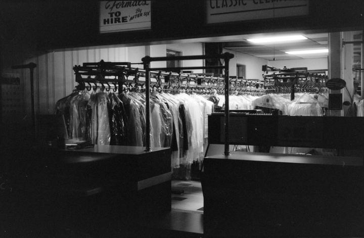 A dry cleaning business is filled with racks of clothes in plastic bags.