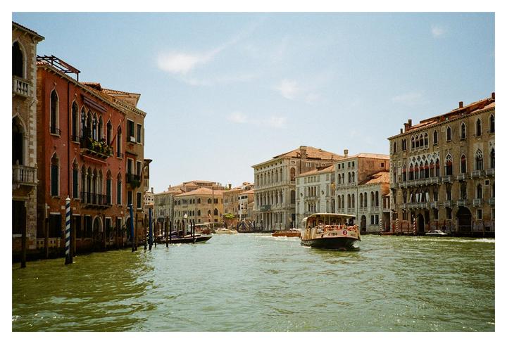 A boat travels down a canal lined with historic buildings under a clear sky.